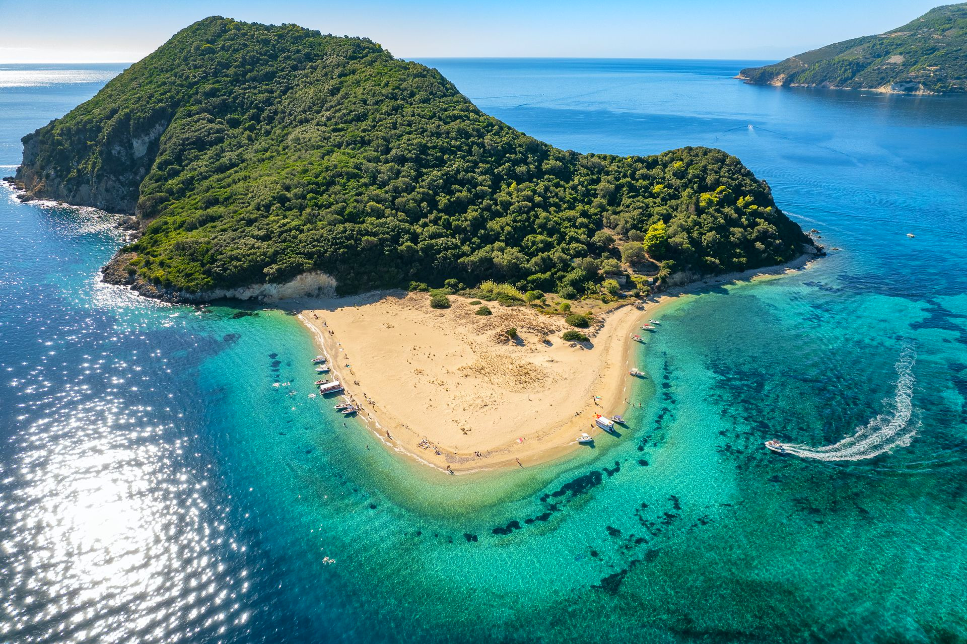 Aerial view of a lush tropical island with a sandy beach, turquoise water, and a blue ocean horizon