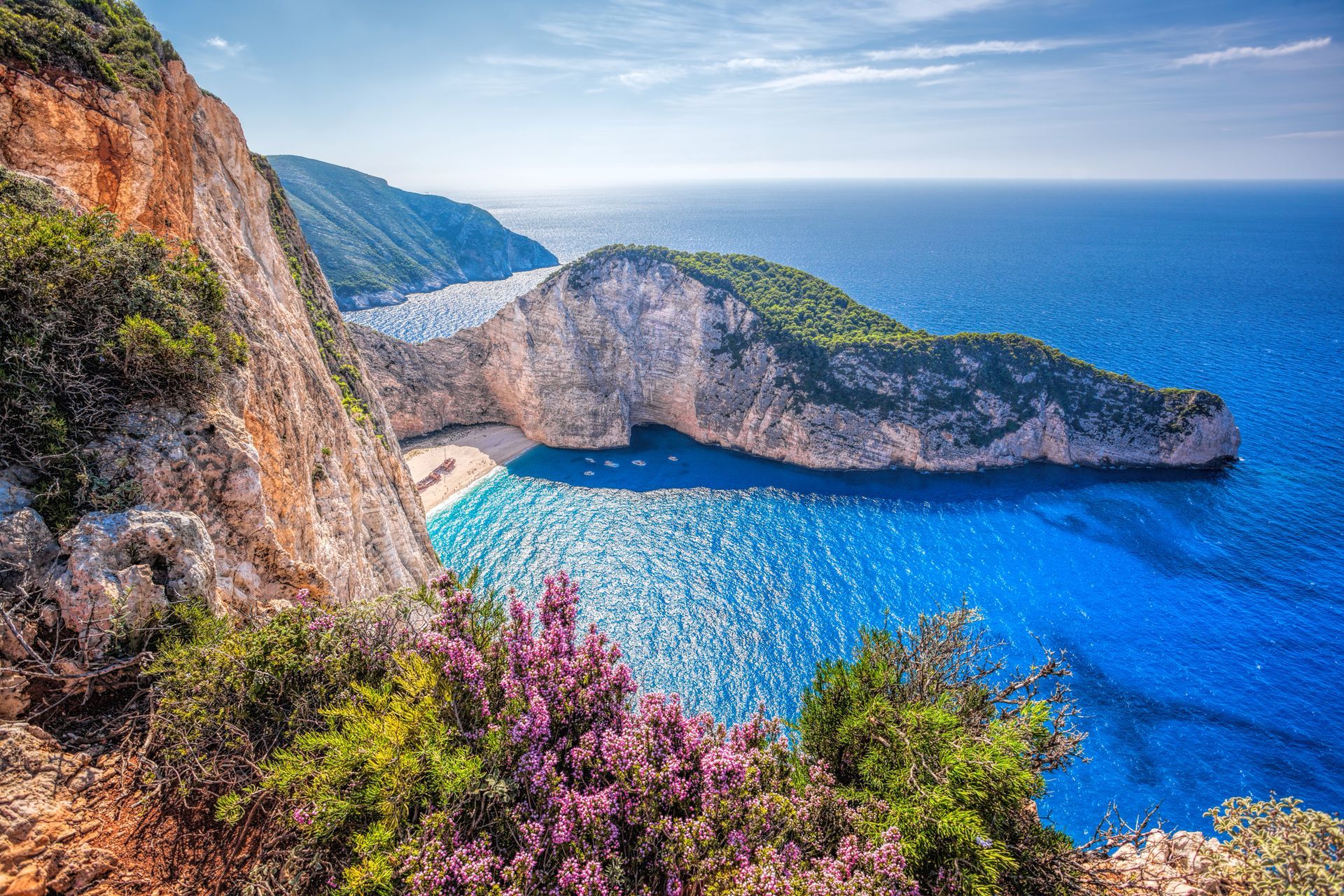 Rocky seaside cliffs above a bright blue bay with wildflowers in the foreground