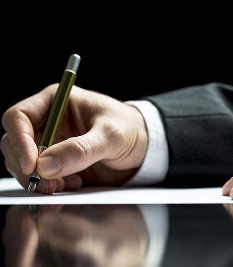 Une main tenant un stylo signe un document sur une table noire réfléchissante.