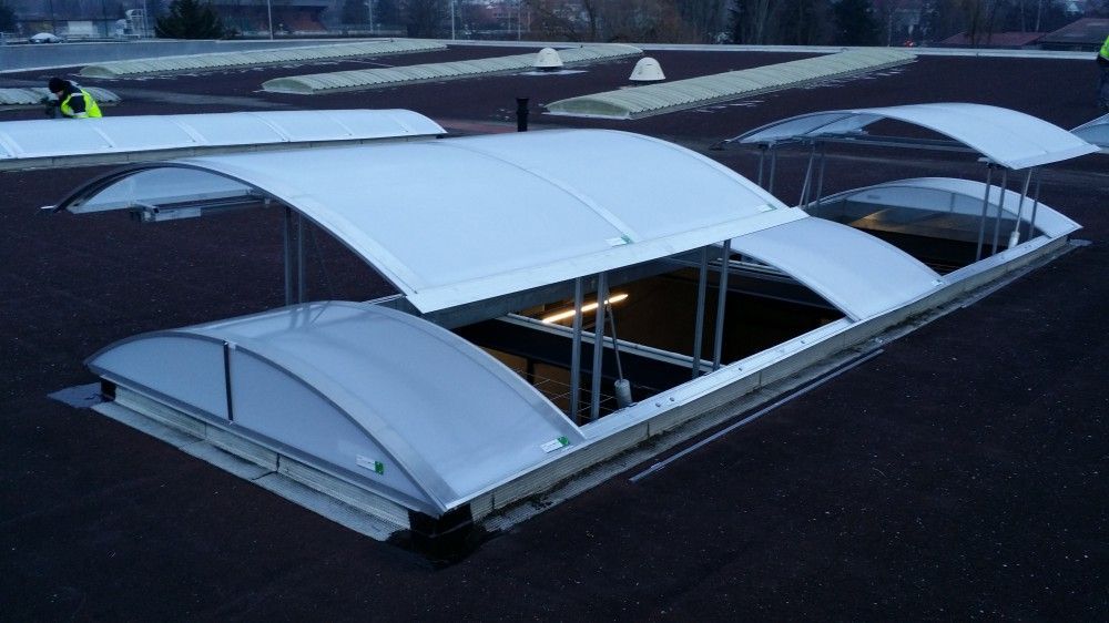 Toit en forme de canopée blanche incurvée recouvrant un parking sombre, vu du ciel.