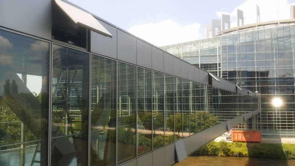 Passerelle moderne en verre avec reflets et cour paysagée baignée de soleil
