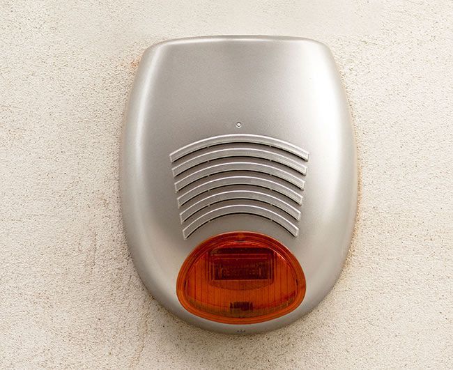 Alarme murale argentée avec lentille orange sur un mur beige