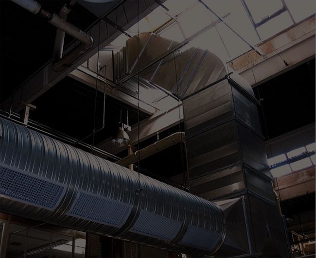Intérieur de style industriel avec de grandes gaines de ventilation argentées et des puits de lumière au plafond.