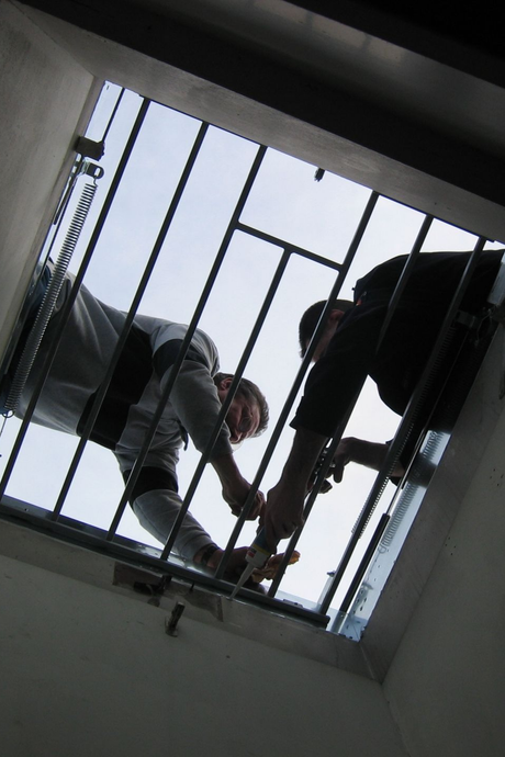 Deux ouvriers sur une grille métallique, vus d'en bas à travers une ouverture au plafond