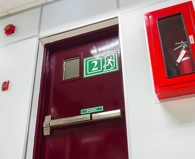 Porte de sortie marron avec panneau de sortie de secours vert et armoire à tuyau d'incendie rouge à côté.