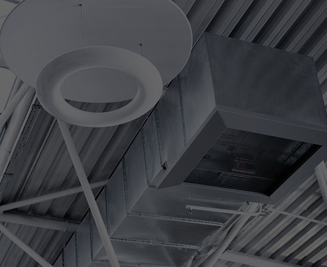 Des grilles d'aération et des conduits fixés au plafond, ainsi qu'un luminaire circulaire, dans un intérieur industriel.
