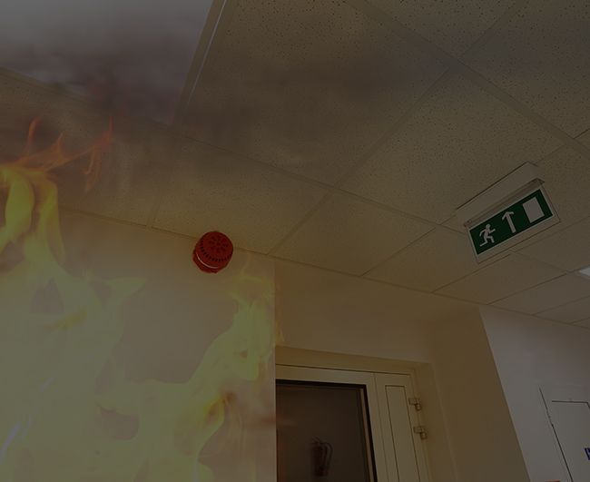 Fumée et flammes près du plafond, alarme rouge et panneau vert de sortie de secours dans un couloir