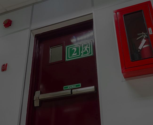 Porte rouge avec panneau de sortie vert et équipement de sécurité incendie fixé au mur.