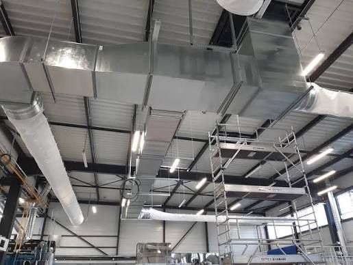 Plafond industriel avec de grandes gaines de ventilation argentées et des poutres métalliques à l'intérieur d'un entrepôt.