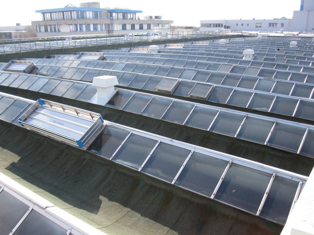 Des panneaux solaires recouvrent un toit sous un ciel lumineux, avec un bâtiment voisin en arrière-plan.