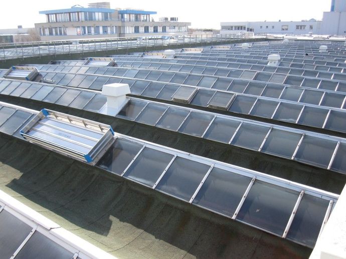 Panneaux solaires photovoltaïques en rangées sur le toit d'un grand bâtiment sous un ciel dégagé, avec des rangées de panneaux réfléchissants