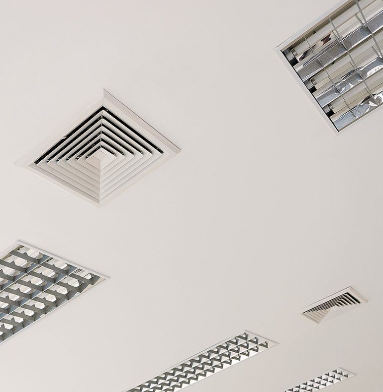 Plafond blanc avec plusieurs grilles de ventilation rectangulaires et panneaux lumineux fluorescents