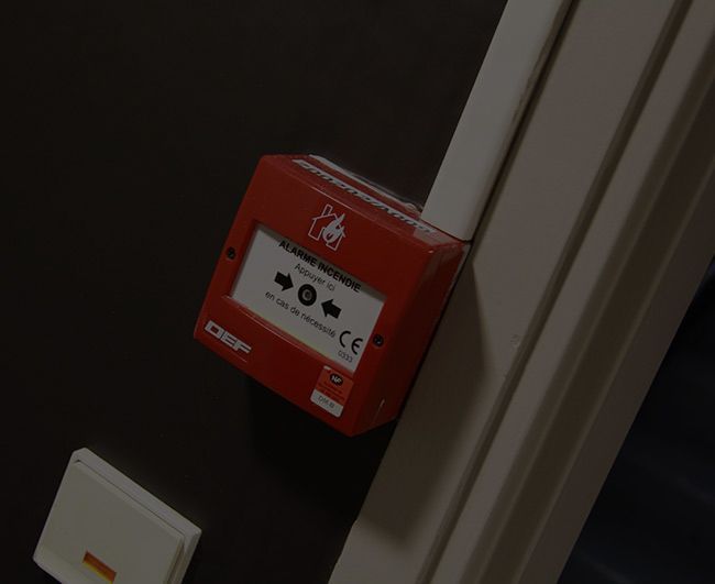 Boîtier d'alarme rouge fixé au mur sur un mur sombre, près d'un cadre de porte blanc