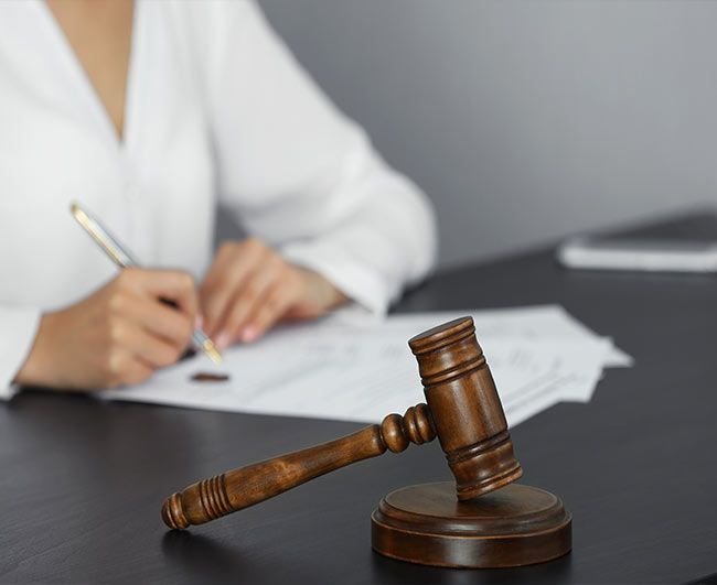 Le marteau d'un juge sur le bureau à côté d'une personne signant des documents dans un bureau