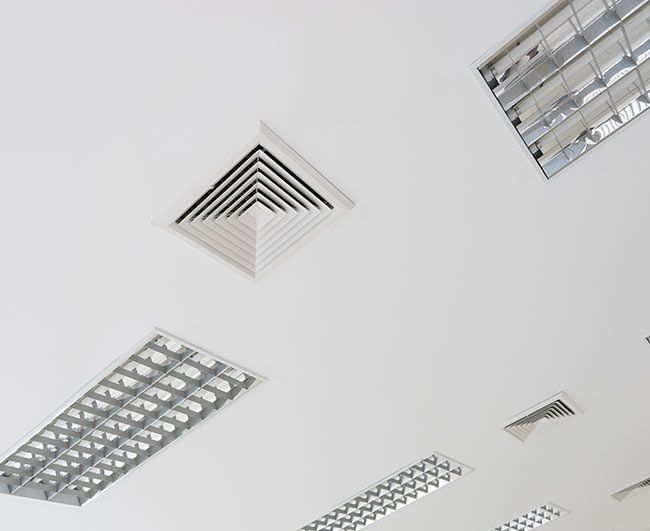 Plafond blanc avec éclairage fluorescent encastré et grilles de ventilation dans un intérieur de type bureau