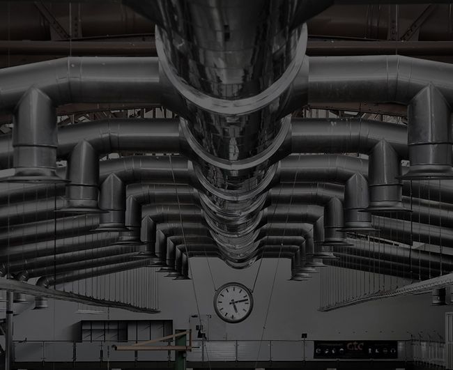 Plafond industriel avec de grandes gaines de ventilation argentées et une horloge murale.