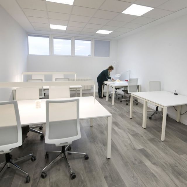 Una mujer se sienta en un escritorio en una habitación con mesas y sillas.