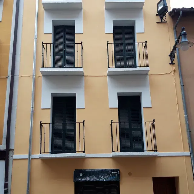 Un edificio amarillo con persianas y balcones negros