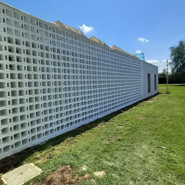 Una gran pared blanca está rodeada de césped y un edificio.