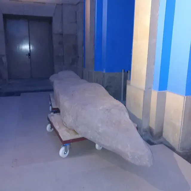 Una gran roca está colocada en un carro frente a un edificio.