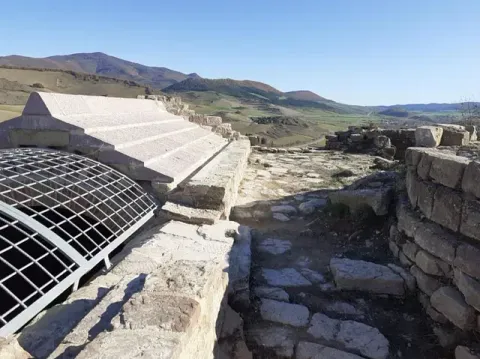 Un edificio muy antiguo con una valla alrededor y montañas al fondo.