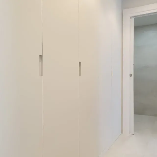 Un pasillo con armarios blancos y una puerta que conduce a un baño.