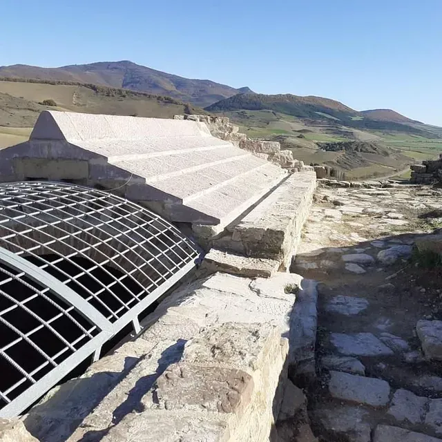 Un muro de piedra con techo de metal y montañas al fondo.