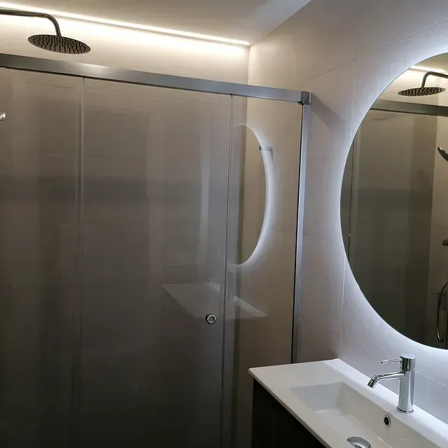 Un baño con una puerta de ducha corrediza de vidrio y un espejo redondo.