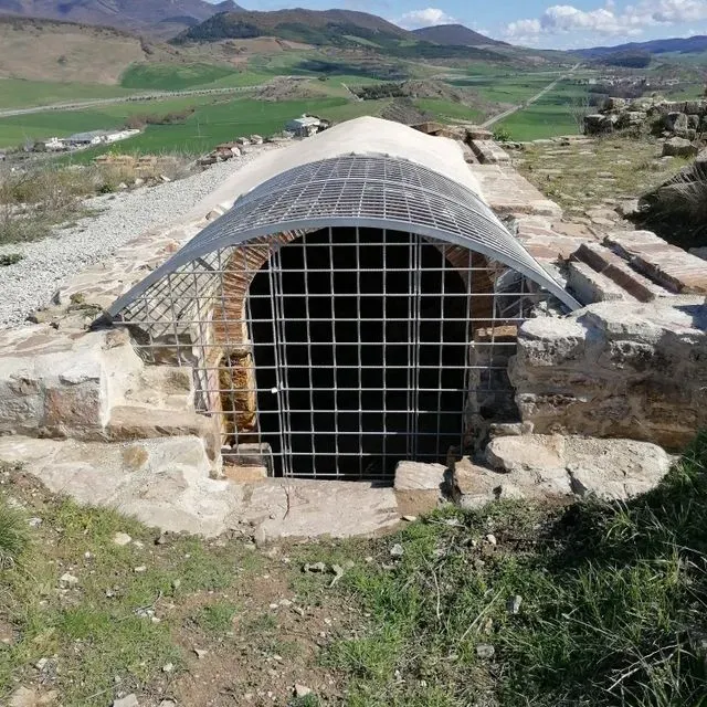 Una cueva con una valla alrededor y montañas al fondo.