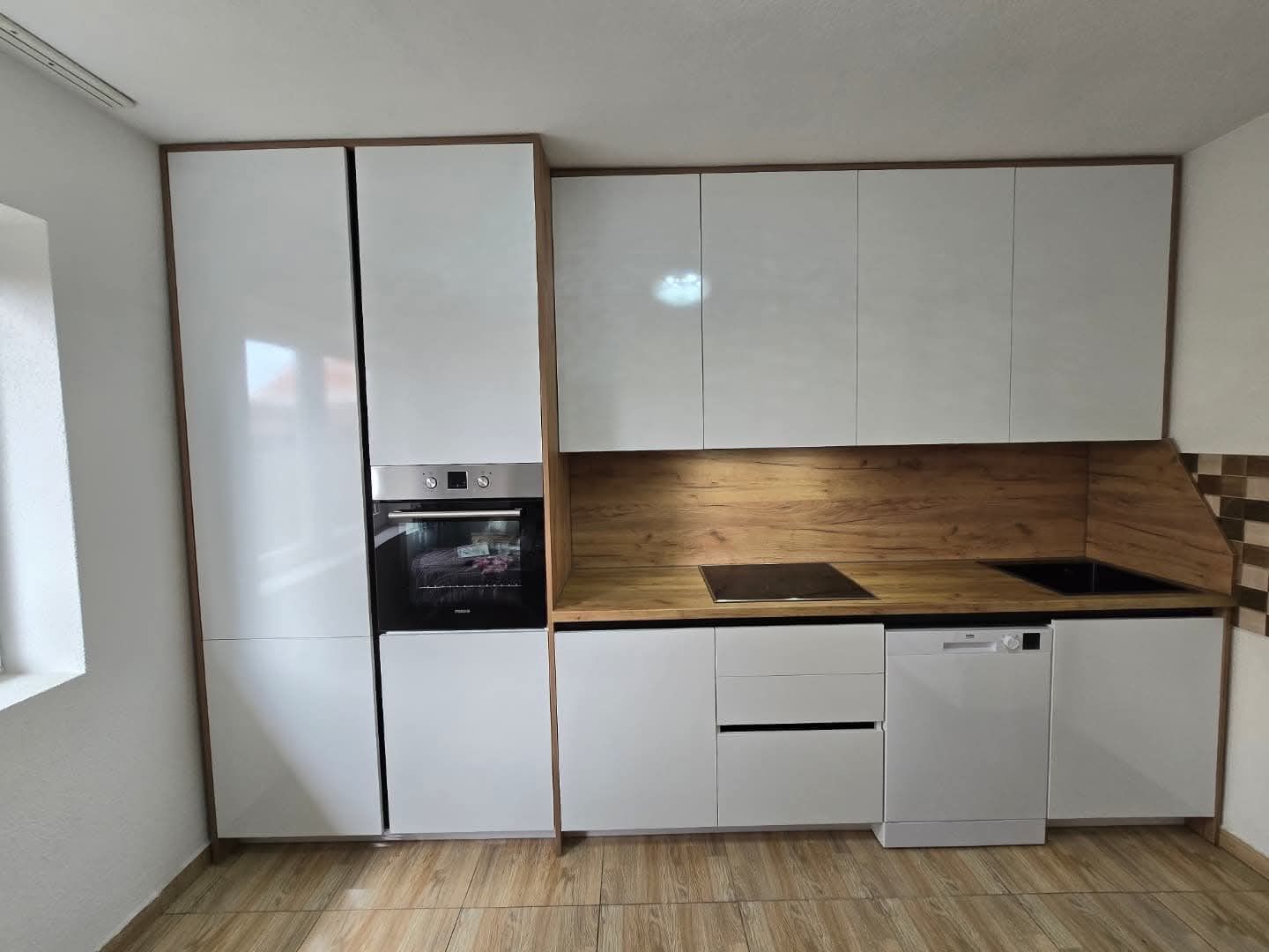Cuisine blanche moderne avec touches de bois. Elle comprend un four encastré, des placards, un lave-vaisselle et une plaque de cuisson.