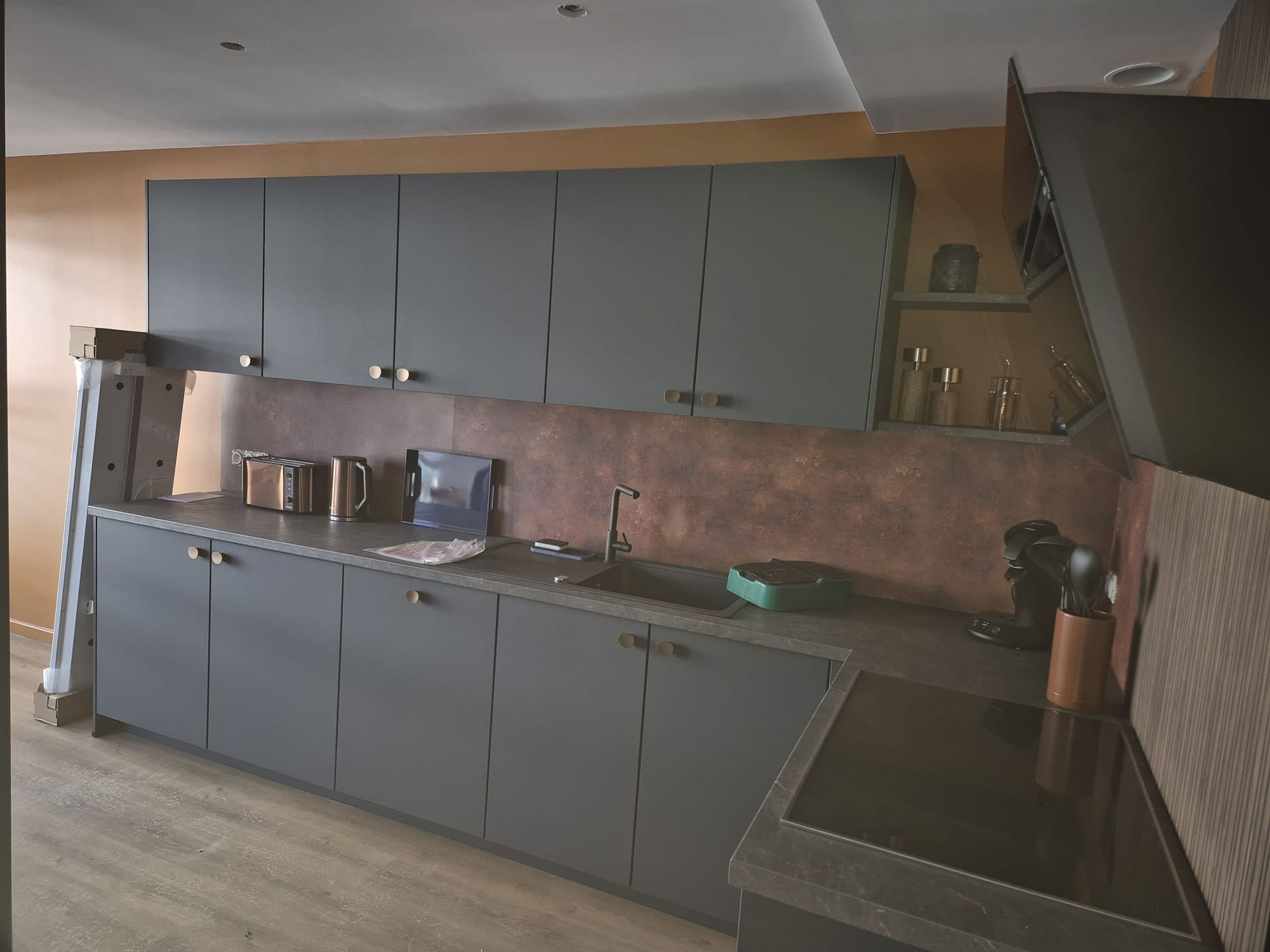 Cuisine équipée d'armoires et de comptoirs gris, d'un dosseret couleur cuivre et d'électroménagers.