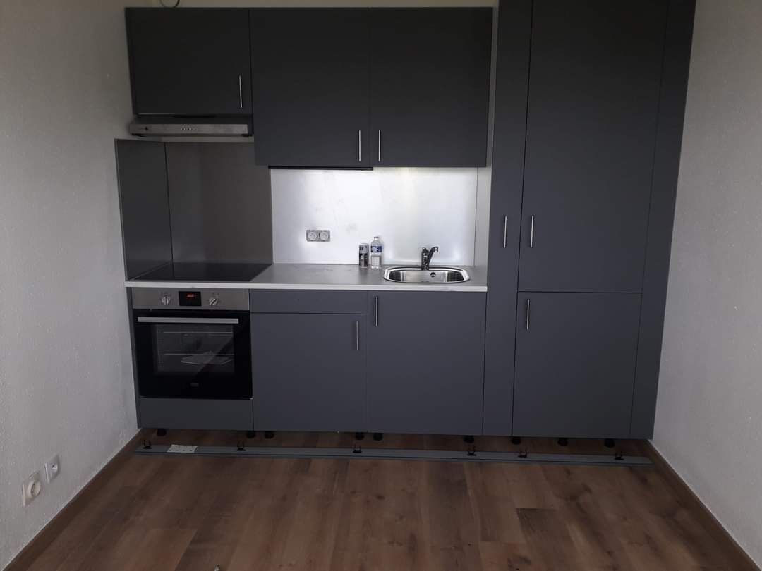Petite cuisine moderne avec placards gris foncé, crédence et électroménager en inox et parquet.
