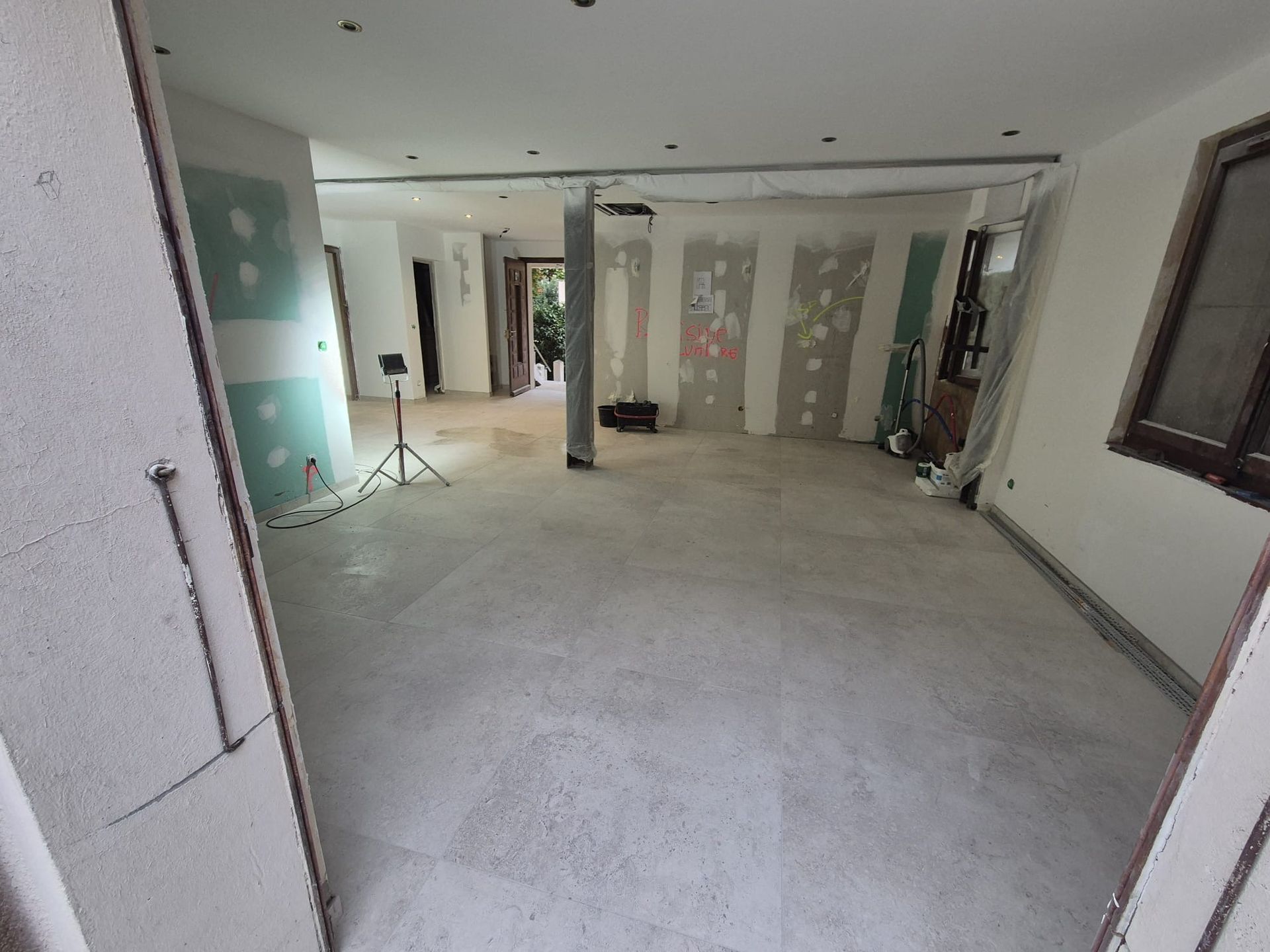 Intérieur en rénovation ; sol en béton, murs apparents, matériaux de construction, porte ouverte.