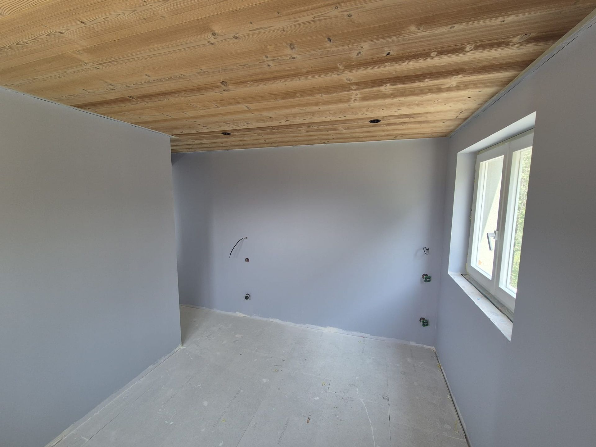 Pièce vide aux murs, plafond et sol gris ; une fenêtre sur la droite.