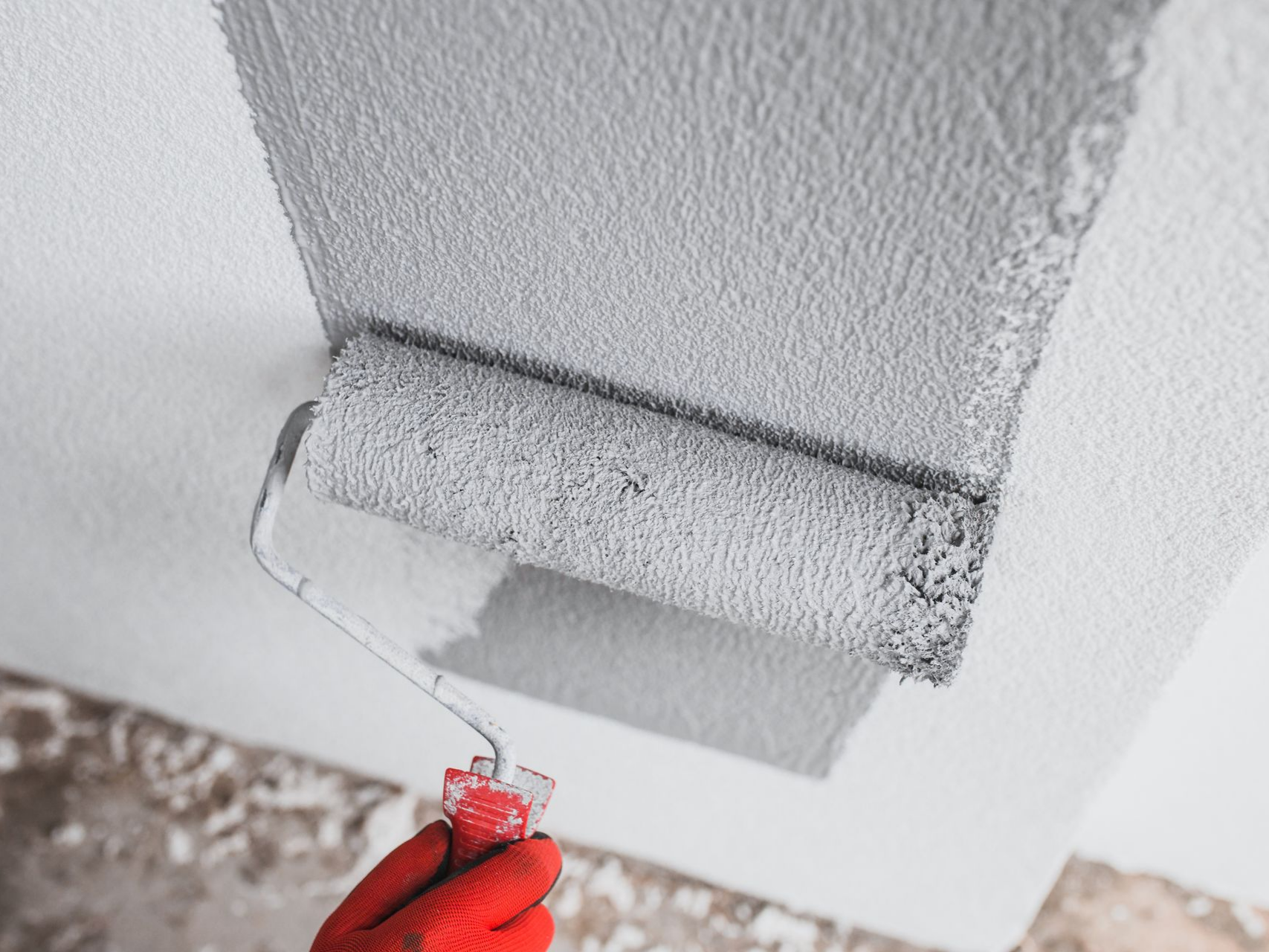 Une main gantée de rouge peint le plafond en gris avec un rouleau.