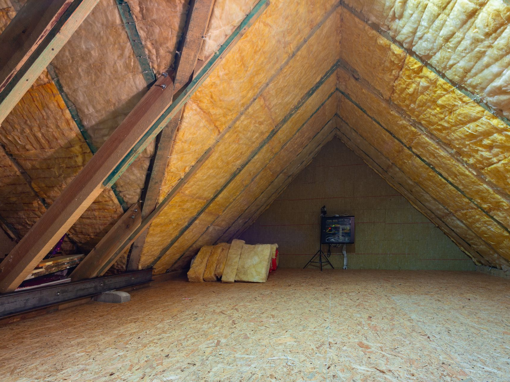 Intérieur du grenier avec poutres en bois, isolation et sol non fini.