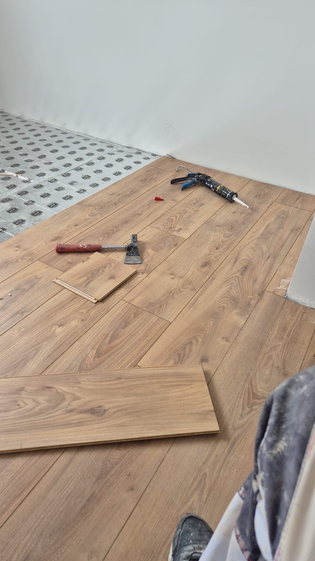 Pose de parquet stratifié : lames, marteau, scie et pose du revêtement de sol dans une pièce.