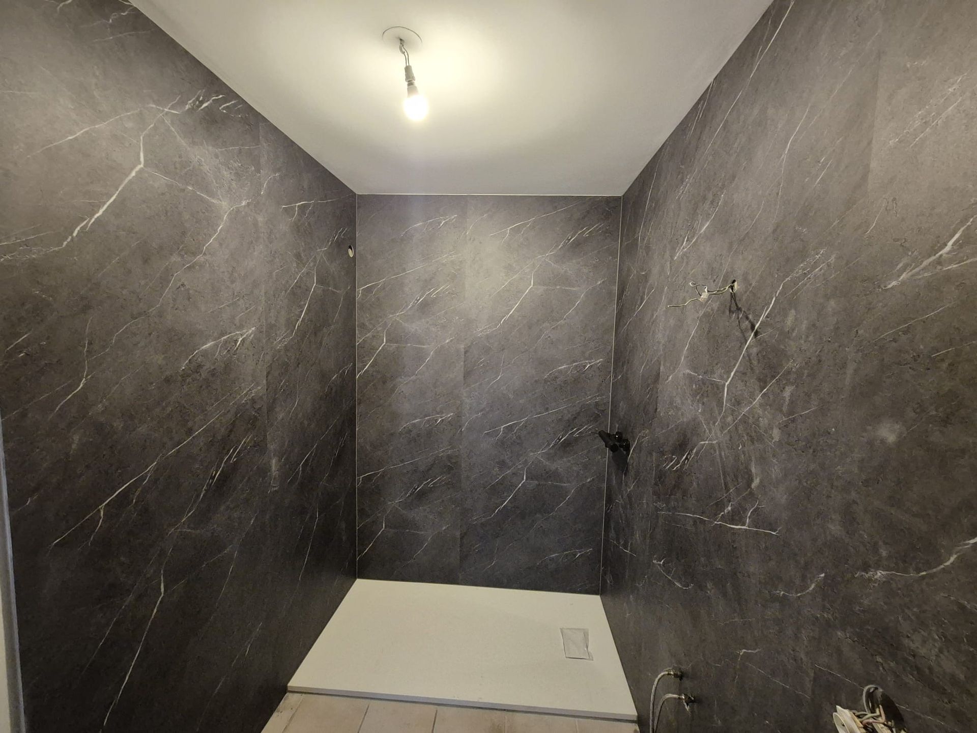 Cabine de douche carrelée gris foncé avec plafond et éclairage blancs, non finie.