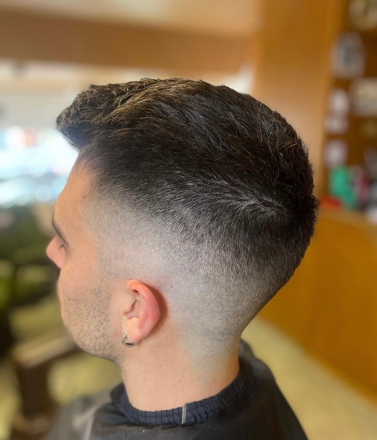 Mann mit dunklem Haar, High Fade-Haarschnitt, Seitenprofilansicht.