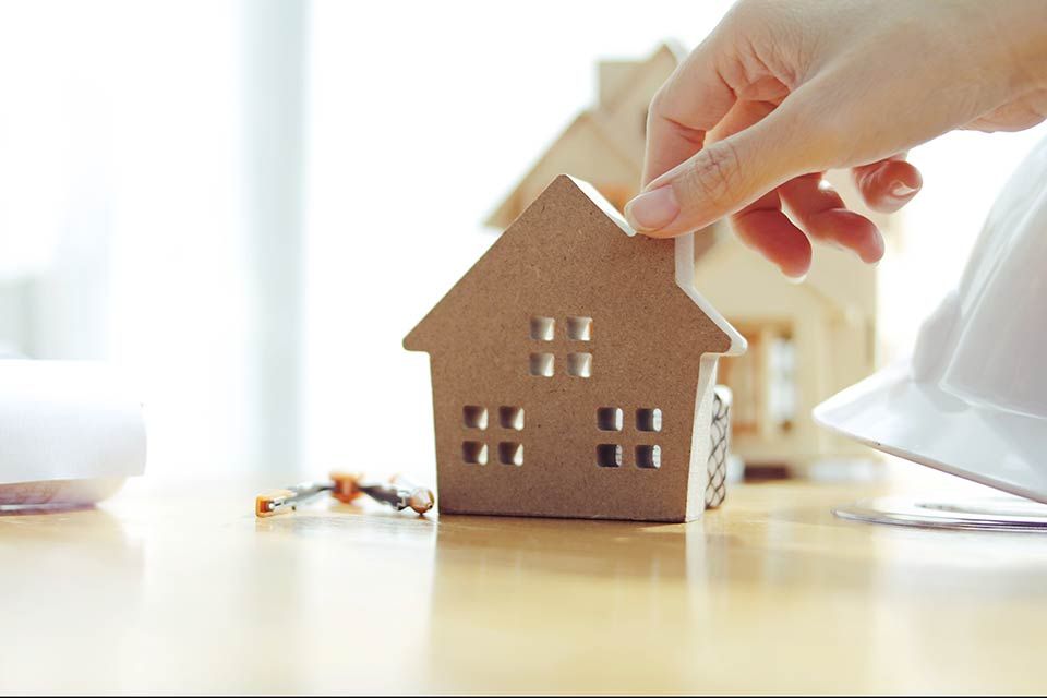 Een persoon houdt een klein modelhuis op een tafel vast.