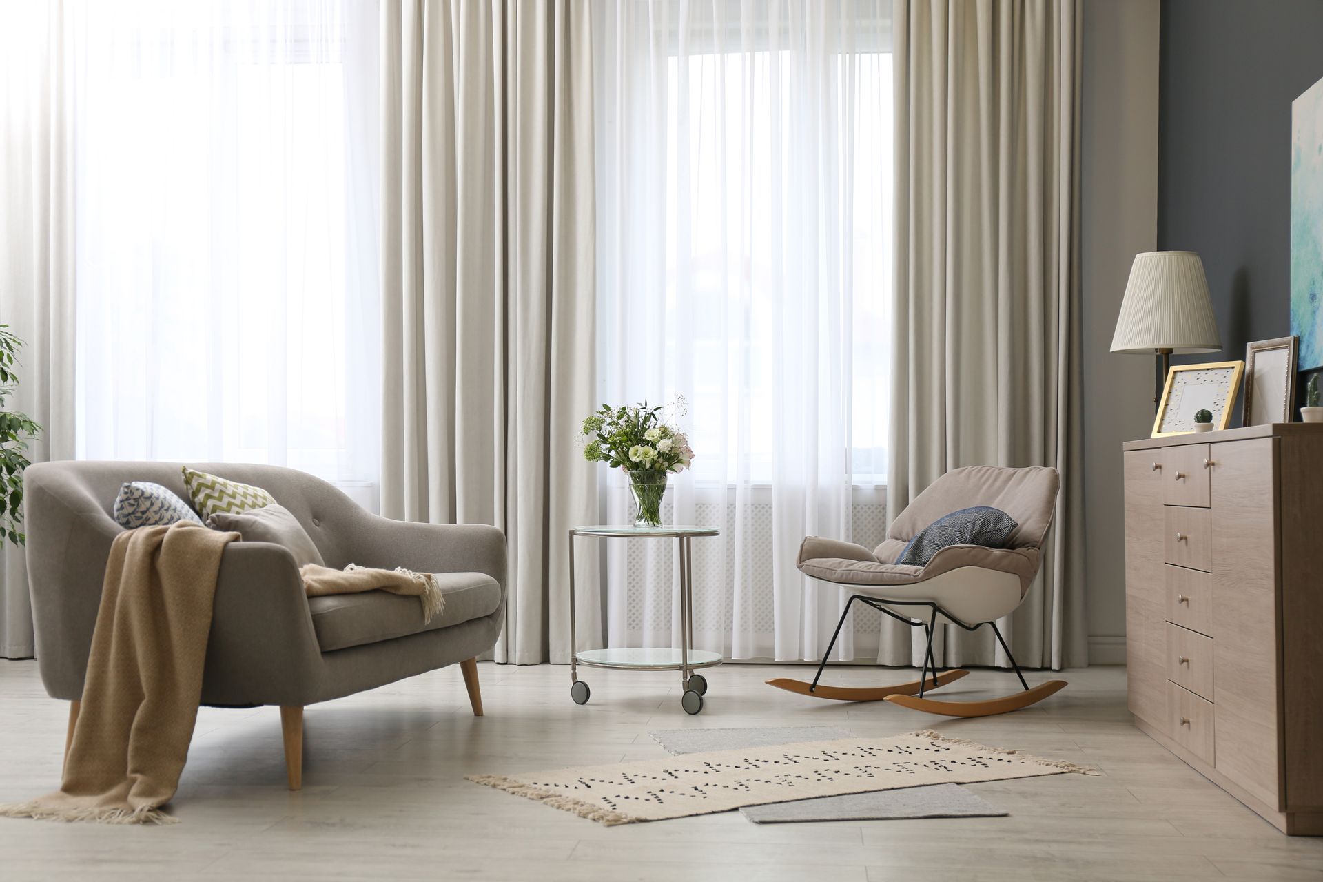 Ein Wohnzimmer mit Couch, Sessel, Vorhängen und Schaukelstuhl