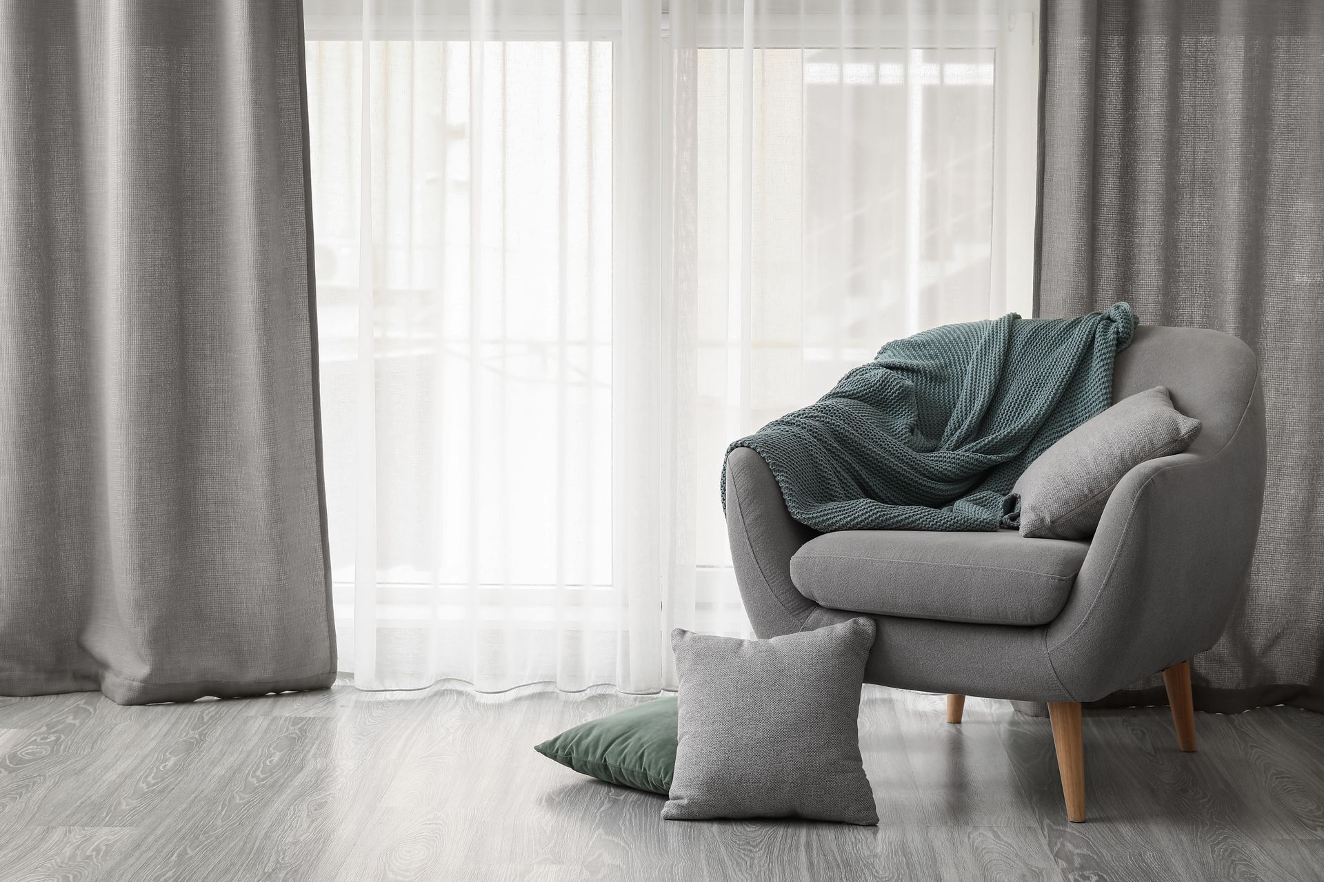 Ein Wohnzimmer mit einem Sessel, Kissen, Vorhängen und einem Fenster