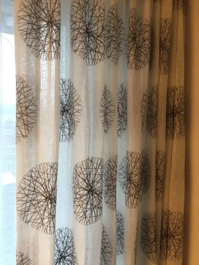 An einem Fenster hängen zwei gemusterte Vorhänge.