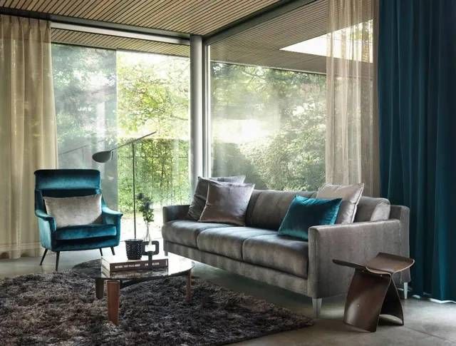 Ein Wohnzimmer mit Couch, Sessel, Tisch und Vorhängen.