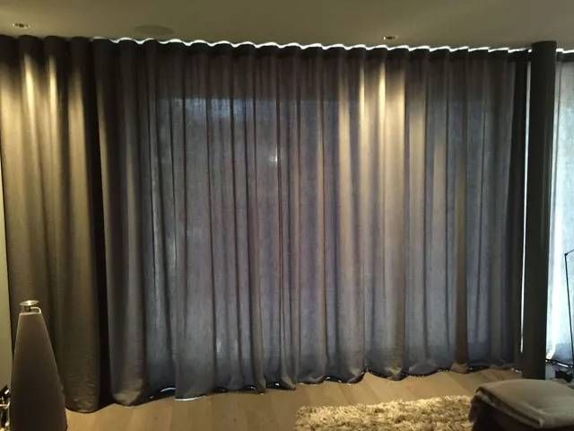 Ein Wohnzimmer mit großem Fenster und grauen Vorhängen.