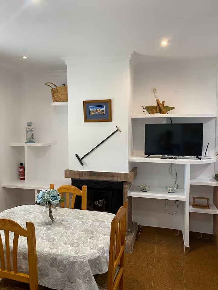 Comedor con mesa, chimenea, estanterías y TV.