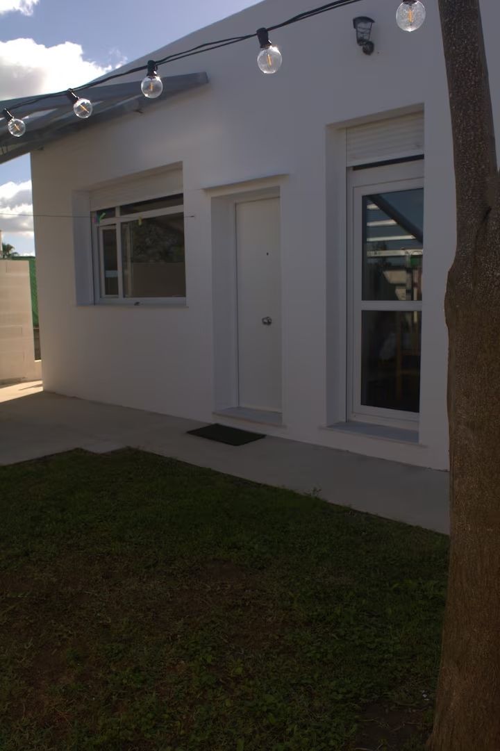 Casa blanca con puerta, ventana y jardín. Guirnaldas de luces cuelgan sobre la entrada.