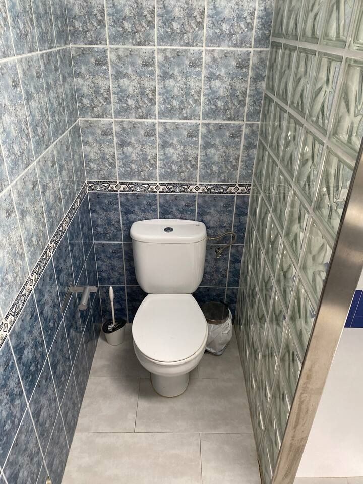 Un baño pequeño con un inodoro blanco, azulejos con dibujos azules y un bote de basura.