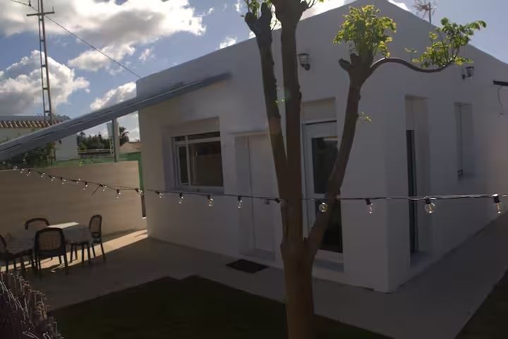 Casa blanca con comedor al aire libre y luces de cadena bajo un cielo azul.
