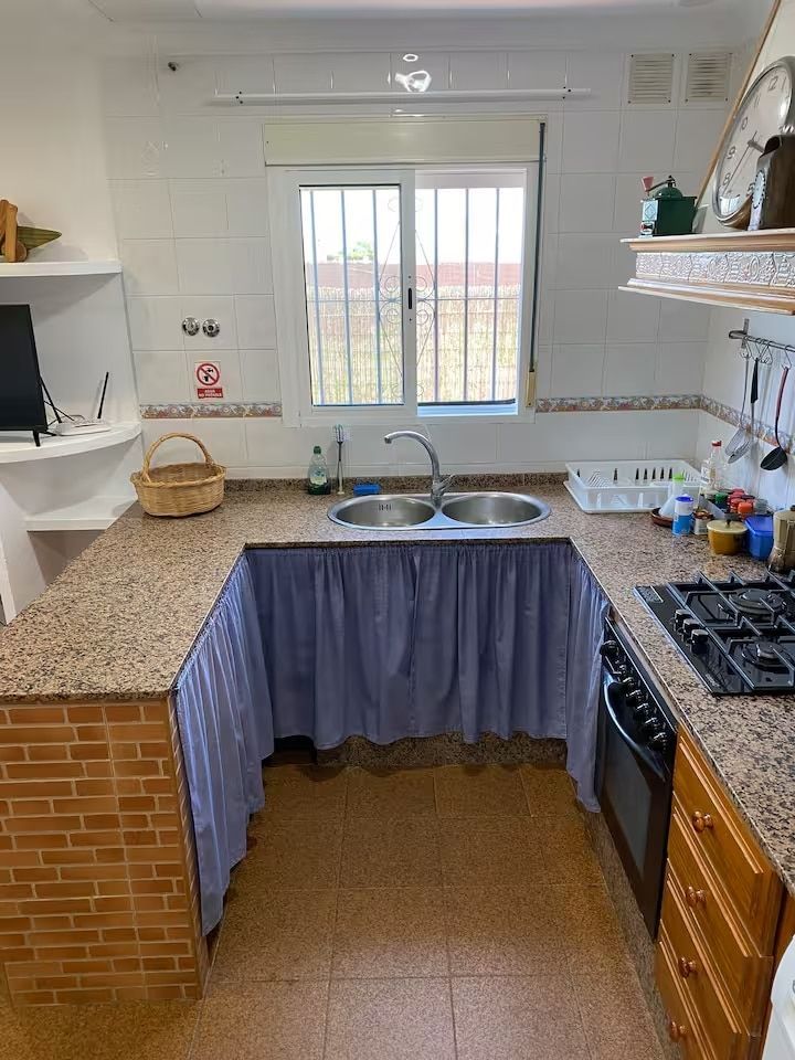 Cocina en forma de U con encimera, fregadero, ventana, estufa y base de gabinete con cortina.